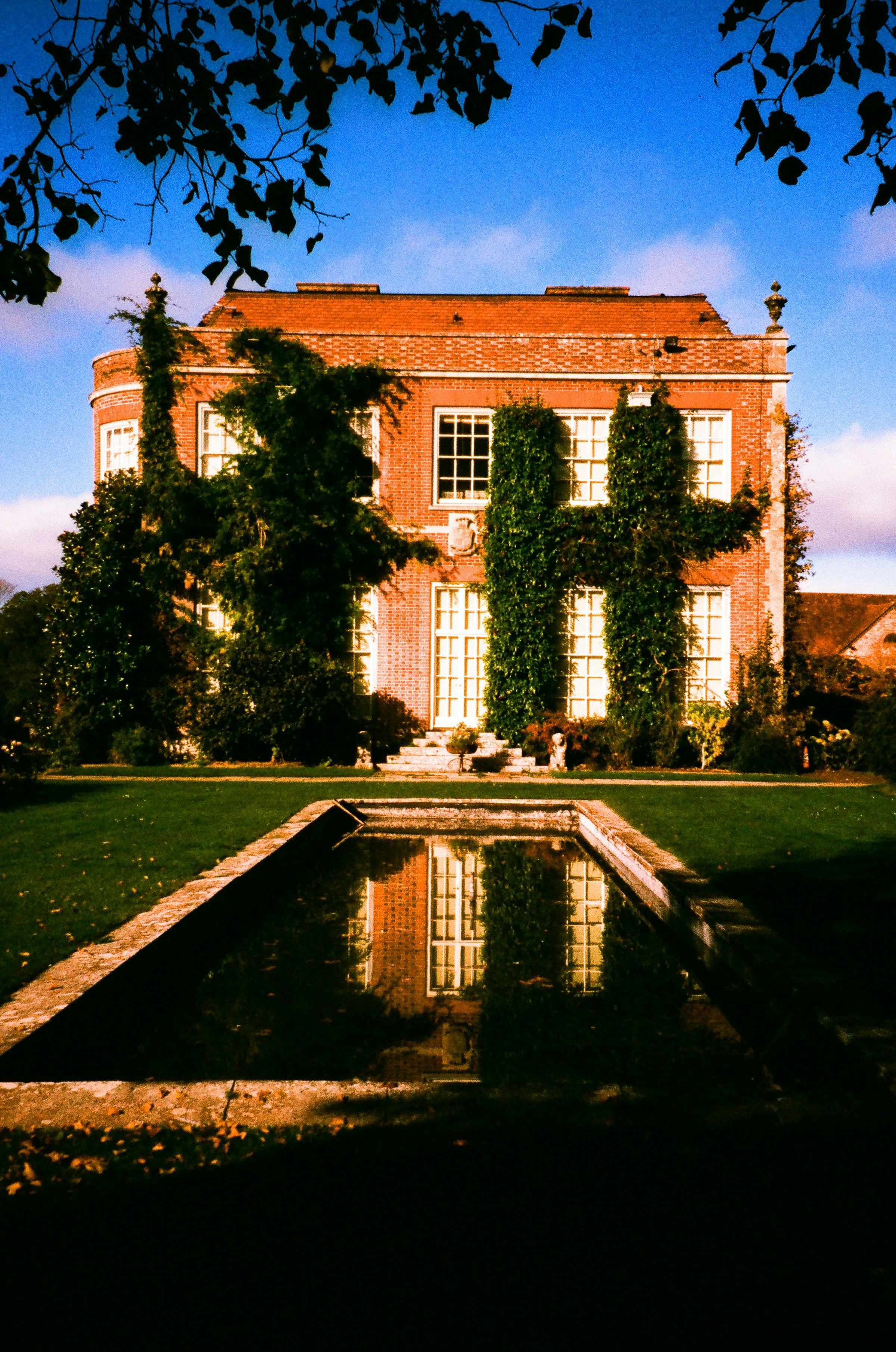 Brick country house with ivy, seen across a still pool at dusk