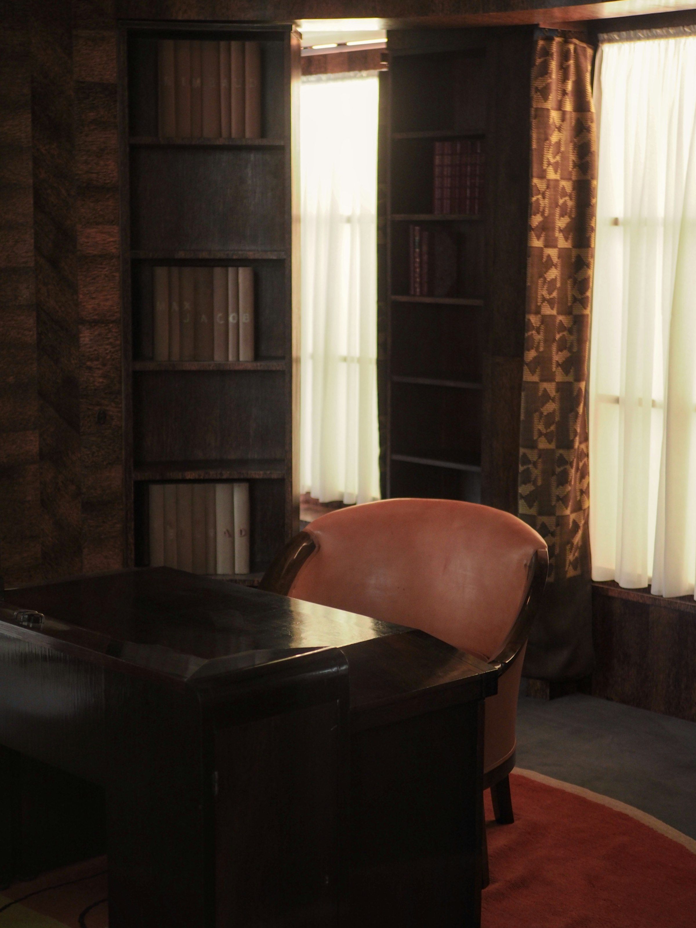 Writing desk and chair beside a curtained window in a panelled room